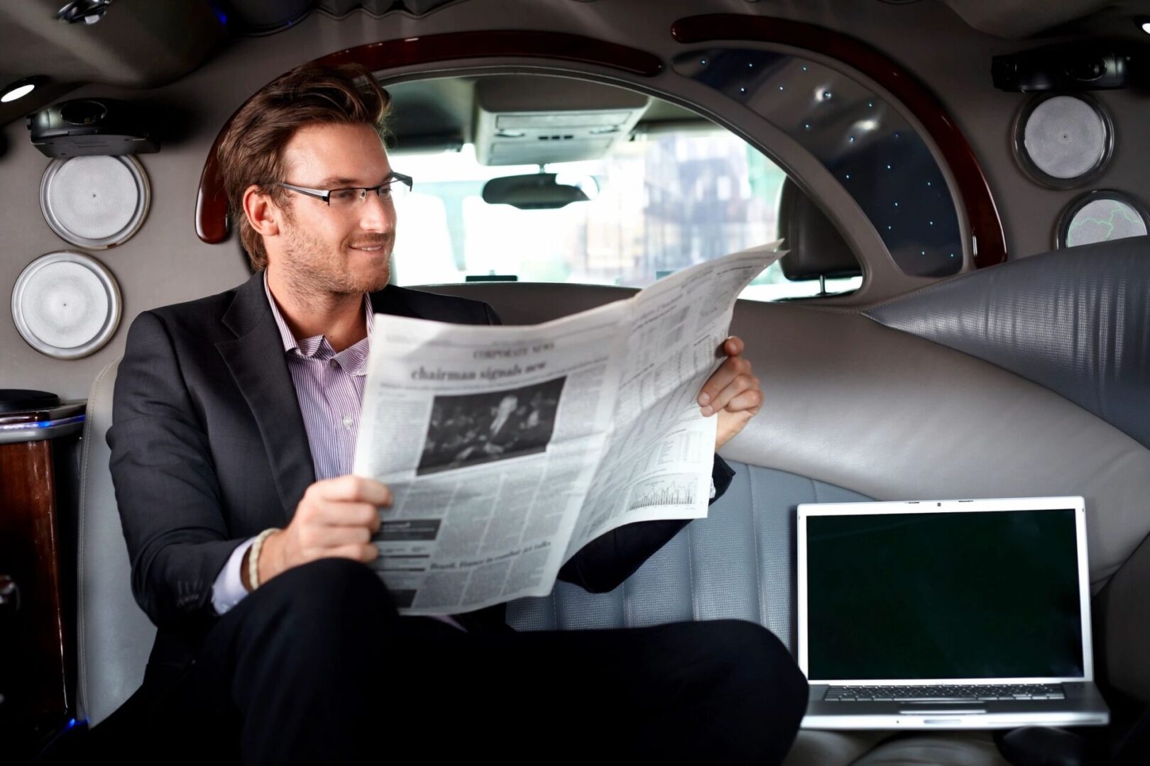 A man sitting in the back of a car reading a newspaper.